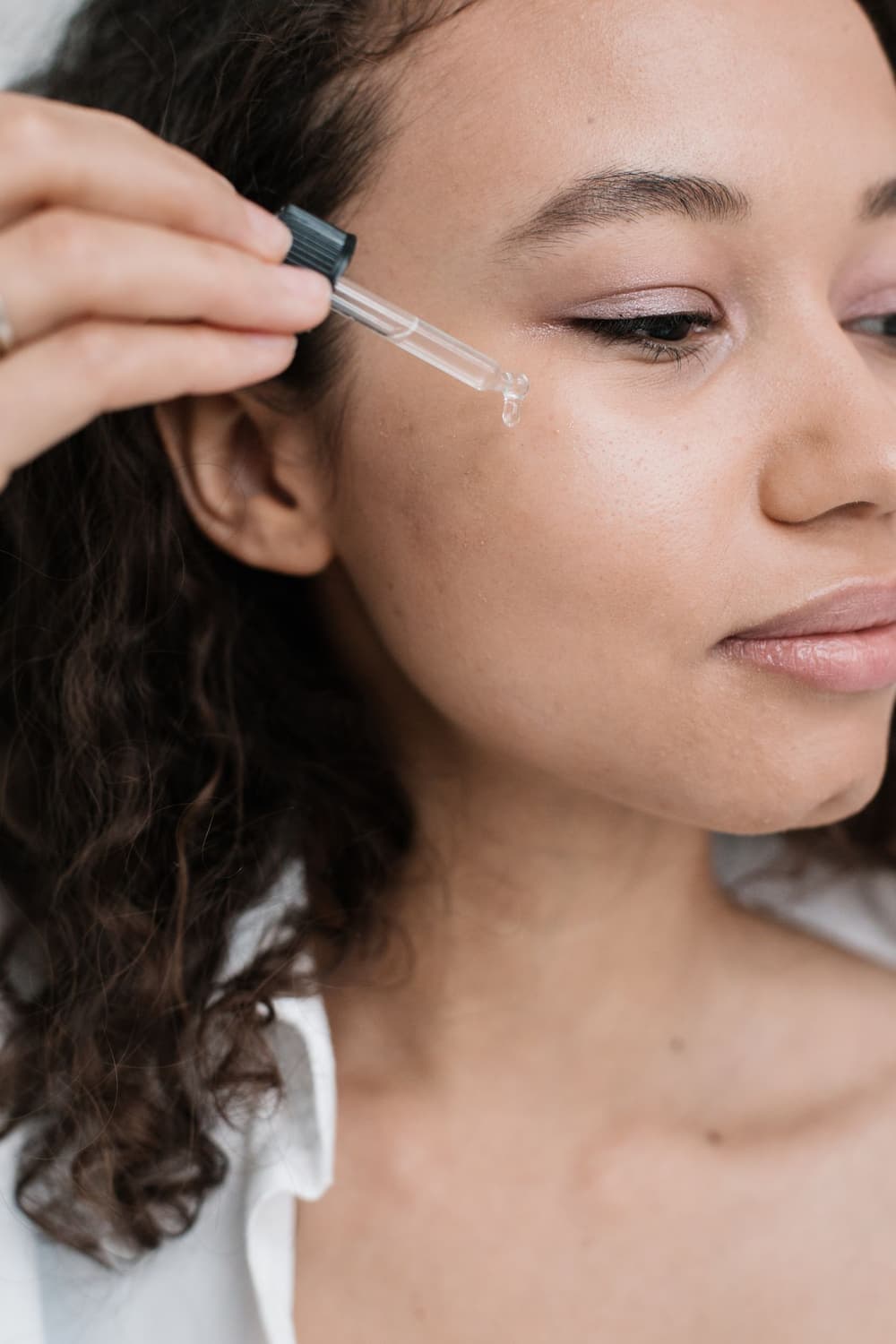 Close-up of a woman applying serum to her cheek with a glass dropper